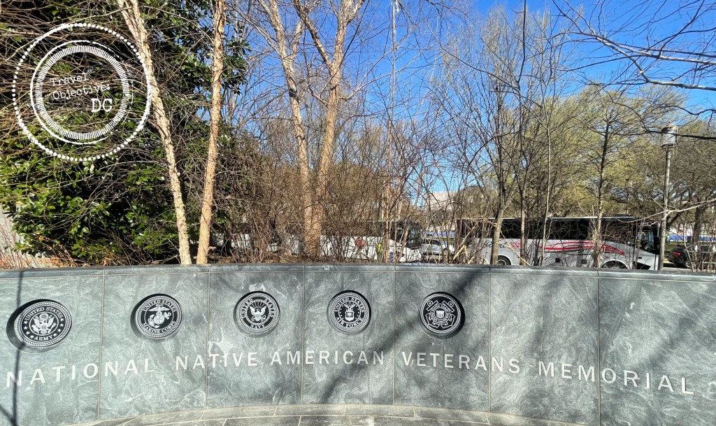 A stone wall with the seals of five of the armed forces marks the entryway to the National Native American Veterans Memorial. 