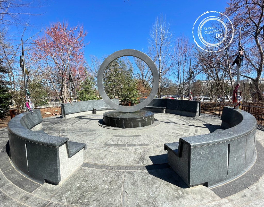 The focus of the memorial is a vertically oriented stainless-steel circle, situated on a carved stone drum surrounded by circular seating area 
