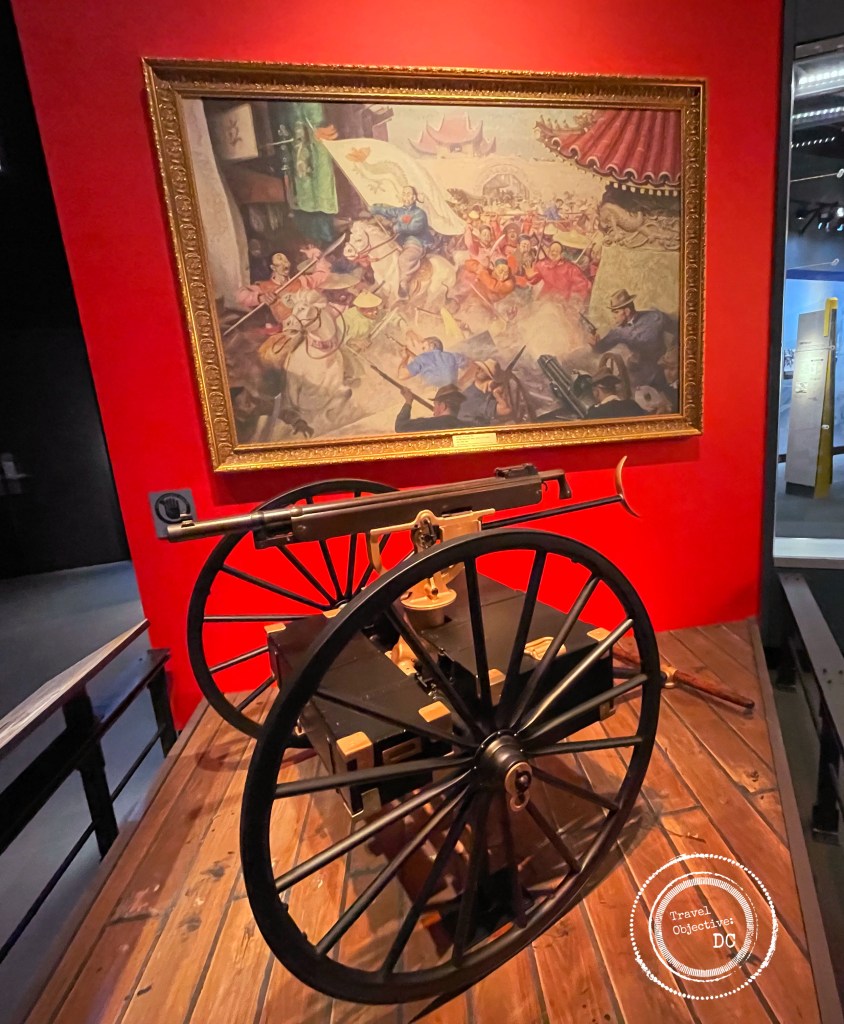M1895 Colt Machine Gun in front of The Defense of Peking-1900 by Staff Sergeant John Clymer, USMCR